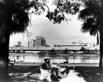 Women seated on riverfront benches in Plant Park with Atlantic Coast Line Freight Depot in background by Burgert Brothers