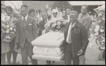 Group of people gathered for a funeral with five men carrying a white casket.