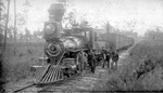 Conductor and workers stand beside a steam locomotive pulling freight cars