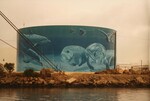 A Citgo gas reservoir painted with an underwater portrait of manateees and other sea creatures stands behind thick cables at the Port of Tampa