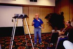 A Florida Ornithological Society member holding a large disk gestures mid-speech during a spring meeting in Tampa, Florida