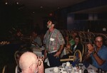 A Florida Ornithological Society presenter stands between tables while the audience claps for another speaker by Florida Ornithological Society