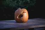 A pumpkin with a bird carved into the side sits atop a picnic table