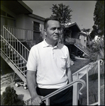 A man leans against a stair railing while standing before a row of elevated houses in Tampa, Florida, B