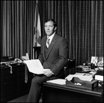 Jerry Bowmer Sitting on Desk with Papers in Hand, A by Skip Gandy