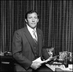 Jerry Bowmer Sitting on Desk with Papers in Hand, I by Skip Gandy