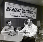 Two Men Sit by Large Banner, Del Monte Corporation, Public Affairs Dept, B by George Skip Gandy IV