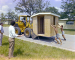 Man Directing Workers Pushing a Shed Lifted by a Bulldozer by George Skip Gandy IV