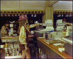 Woman Tending Bar and Operating Cash Register, K by Skip Gandy