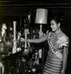 Miss Universe by Shelves with Vases, Lamps, and Other Decorations at JM Fields by George Skip Gandy IV