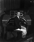 An Organist poses in front of an organ and a microphone