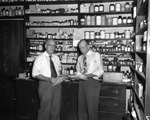 Pharmacists Standing in Front of a Wall of Medications by Robertson and Fresh