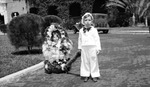 Boy pulling a girl in small flower-draped parade float; car in background