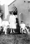 Bulletin board photo of photo of young girl with spotted dog, two women, and seated man on grass outside building(s) number 2118? with striped awnings