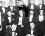 Bulletin board photo of photo of posed group of men in tuxedos and sashes; three rows of men, tall windows, wood floor-possibly taken in a ballroom