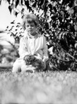 Betty sitting in grass, holding Uppy the puppy and looking down by Francis G. Wagner and Nelson Poynter Memorial Library