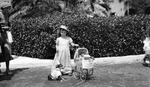 Girl in long dress and matching hat, costumed dog, and doll carriage with sign, "St. Pete Future Housewife." Woman at far left; probably taken at the Vinoy Hotel by Francis G. Wagner and Nelson Poynter Memorial Library