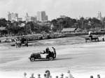 Car with sign "Welcome Santa Claus," small airplanes parked, large crowd of people, downtown St. Petersburg in background including Princess Martha, Central National Bank and Trust Co., other tall buildings by Francis G. Wagner and Nelson Poynter Memorial Library