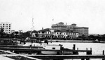 Esther Stewart Kahn photo of St. Petersburg Yacht Club from the water, including some boats, docks, people, many cars. Soreno Hotel looming behind, part of Ponce de Leon Hotel on left. Writing on the back of photo identifying buildings by Francis G. Wagner and Nelson Poynter Memorial Library
