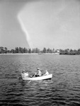 Four people in a rowboat in the middle of the water, foliage and settlement in background by Francis G. Wagner and Nelson Poynter Memorial Library