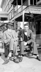 Francis and unknown younger man in three piece suits sitting on bench in front of Southern Trunk and Umbrella Works by Francis G. Wagner and Nelson Poynter Memorial Library