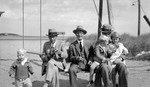 Wagner family in coats at a beach swingset in Maine. Bud stands in front of Jesse, who holds a camera, Octavus Talpey in middle, Francis holds Betty, who wears an Indian costume, and Dick, who holds a feather fan by Francis G. Wagner and Nelson Poynter Memorial Library