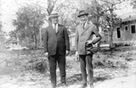 Two unknown men with hats standing in large yard with houses in background by Francis G. Wagner and Nelson Poynter Memorial Library